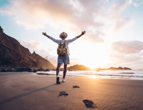 Young man arms outstretched by the sea at sunrise enjoying freedom and life, people travel wellbeing concept